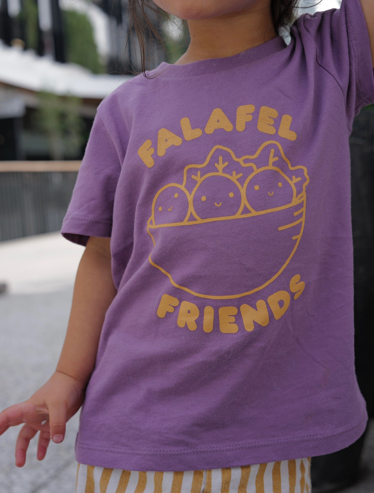 Child wearing a purple t-shirt with 'Falafel Friends' design outdoors.