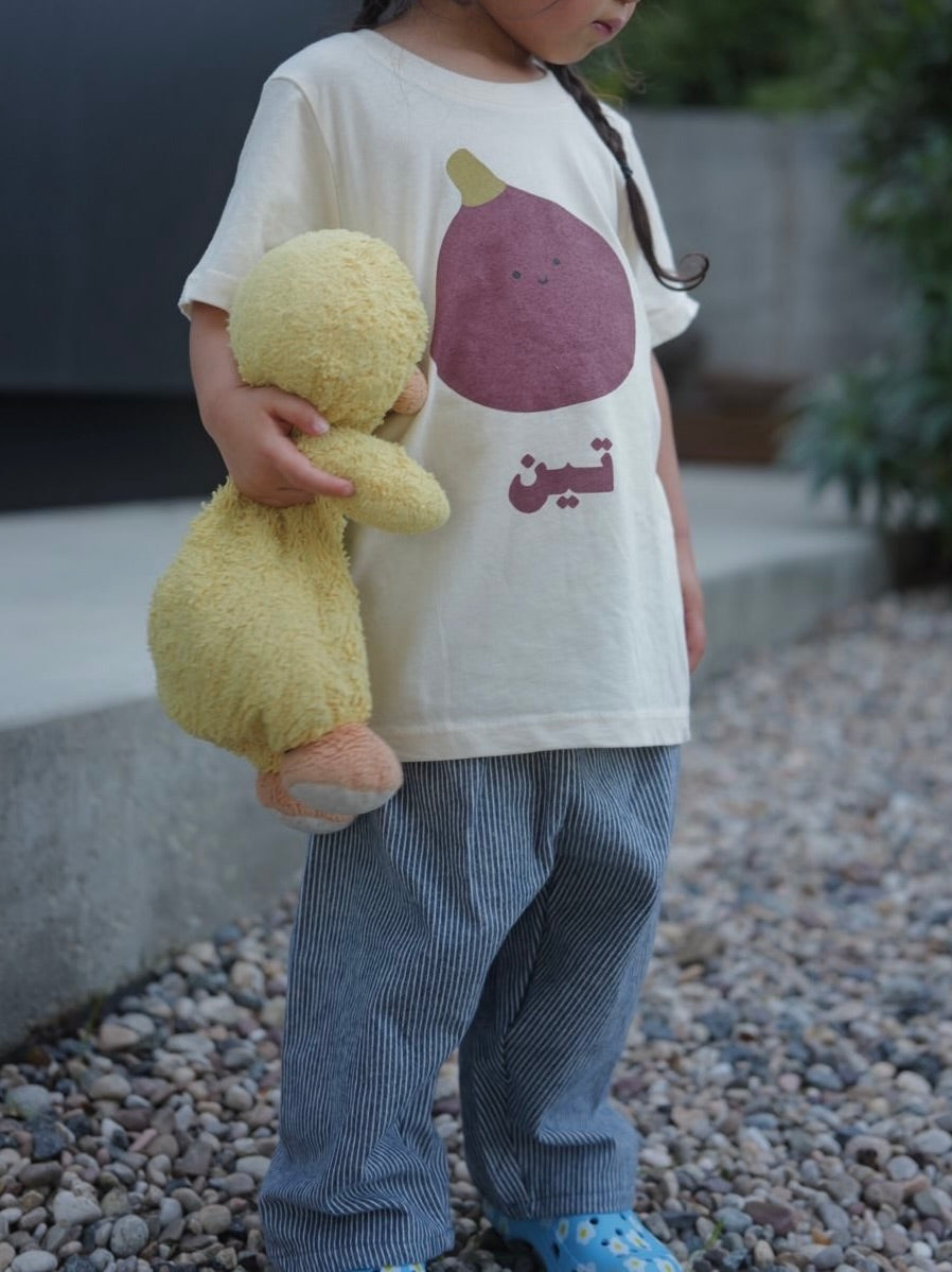 Child holding a yellow teddy stuffed animal wearing a white t-shirt with a fig design.