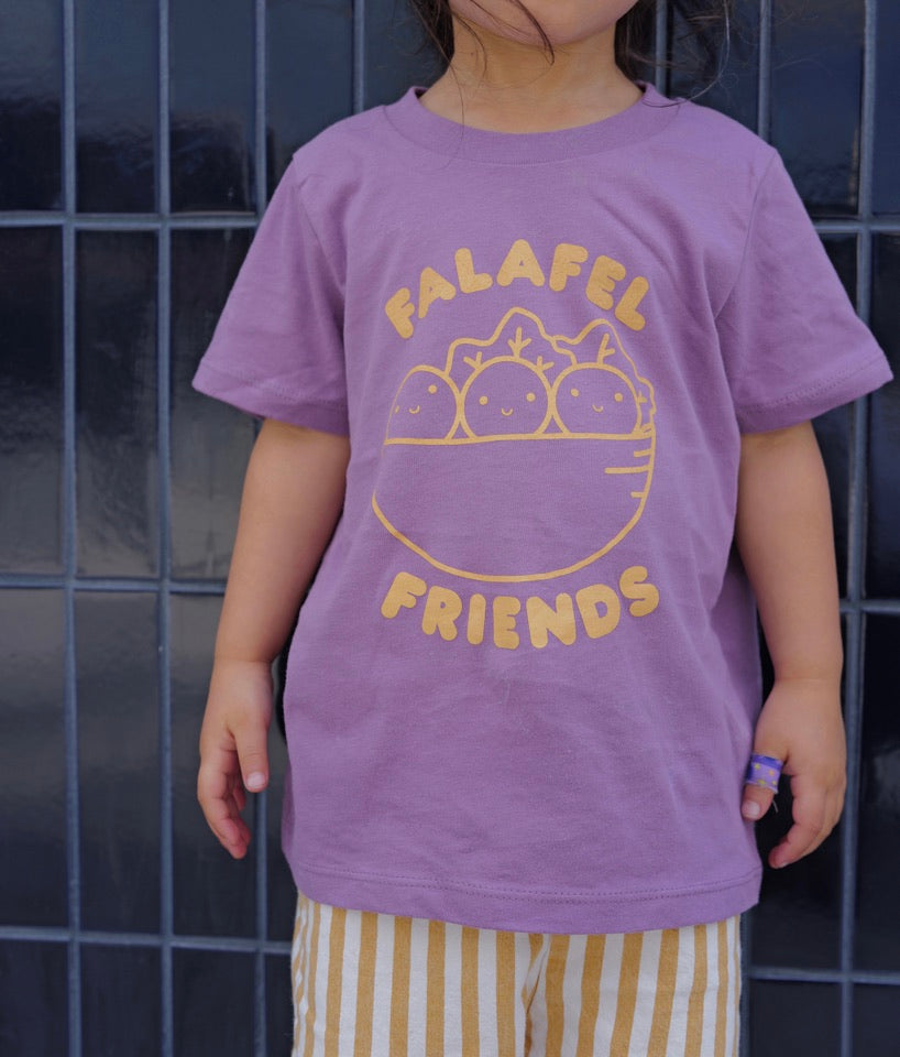 Child wearing a purple t-shirt with 'Falafel Friends' design against a tiled wall.