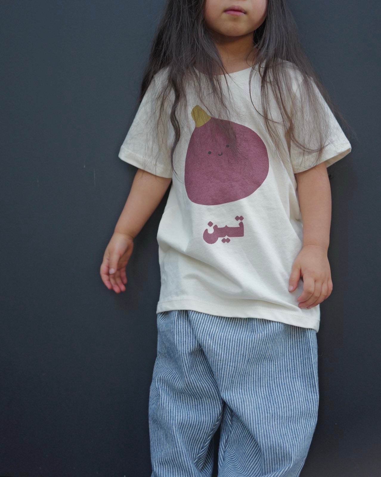 Child wearing a t-shirt with a purple fruit graphic and text against a dark background