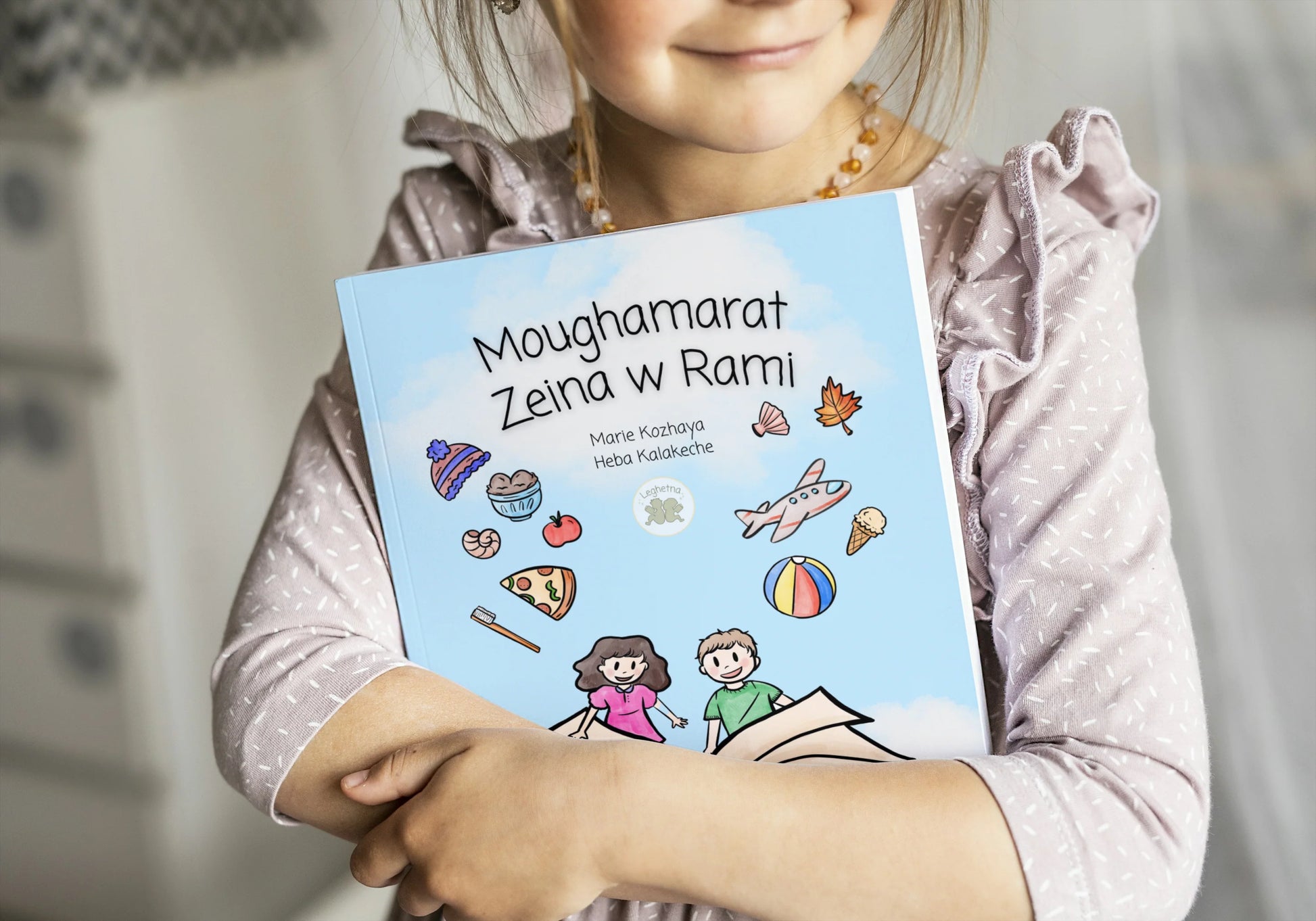 Child holding a book titled 'Moughamarat Zelina w Ramli' with colorful illustrations on the cover.