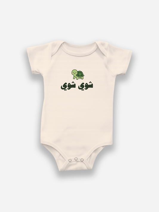 Beige baby onesie with a green turtle design and arabic text on a white background