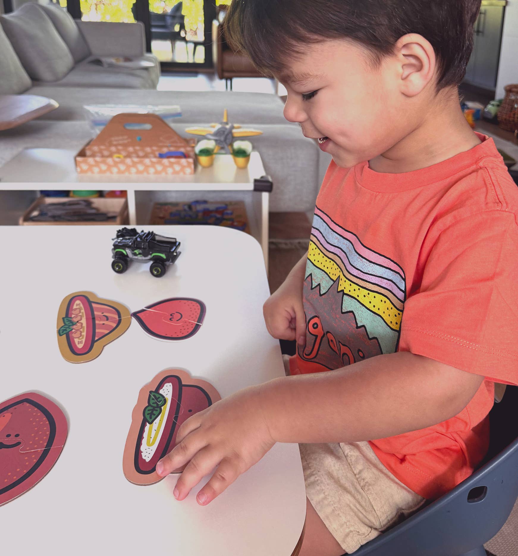 Child playing with toy vehicles and colorful paper cutouts on a table.